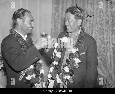 Toast auf eine großartige Platte. Japanische Flieger schließen Rekordflüge über 10,000 Meilen ab. Nachdem die japanischen Piloten Masaaki Iinuma und Kenji Tsukakoshi alle Rekorde mit dem Flug von 10,000 Meilen von Tokio nach London in gut 100 Stunden zerschlagen hatten, landeten sie Croydon in ihrem Flugzeug Divine Wind [Mitsubishi Ki-15 Karigane Aircraft, Name: Kamikaze, Registration J-BAAI]. Die Flyer haben Krönungsgrüße aus Japan mitgebracht. Foto zeigt: Der japanische Flieger Masaaki Iinuma (rechts) der 27-jährige Pilot und sein Funker Kenji Tsukakoshi tauschen nach telefonischen Glückwünschen Champagner-Toast aus Stockfoto