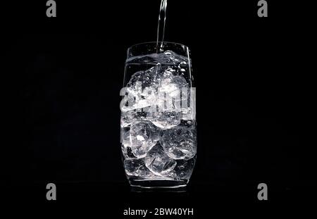 Wasser in Glas mit zerkleinertem Eis auf schwarzem Hintergrund gießen Stockfoto
