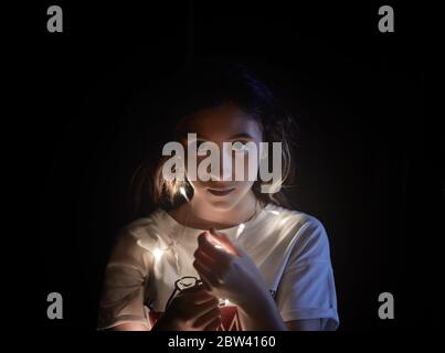Mädchen mit LED-Licht auf ihren Händen in einem dunklen Hintergrund mit weißem T-Shirt Blick auf die Kamera. Selektiver Fokus Stockfoto