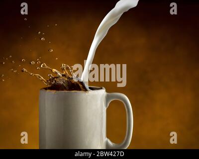 Milch wird in Kaffee gegossen, so dass Kaffee spritzt Stockfoto