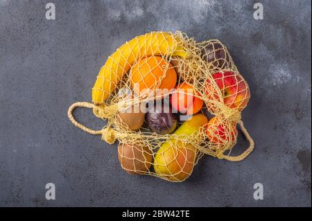Früchte im Sortiment in gelber Öko-Saitentasche auf dunkler Holzoberfläche. Konzept des Umweltschutzes. Kopierbereich Stockfoto