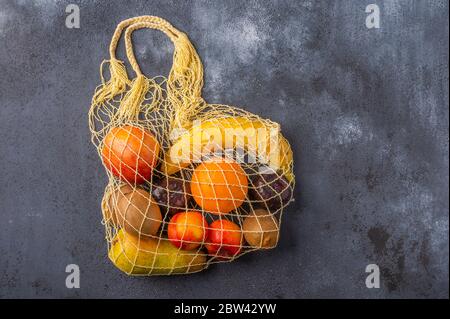 Früchte im Sortiment in gelber Öko-Saitentasche auf dunkler Holzoberfläche. Konzept des Umweltschutzes. Kopierbereich Stockfoto