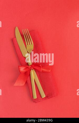 Gold Besteck auf rotem Hintergrund. Saint Valentines Tag Feier oder romantisches Abendessen minimales Konzept. Stockfoto