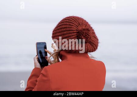 Mädchen mit rotem Mantel und einem roten Hut von ihrem Rücken, berühren ihr Handy. Junge Frau, die ihr Handy. Mädchen trägt einen roten Hut und roten Mantel. Stockfoto