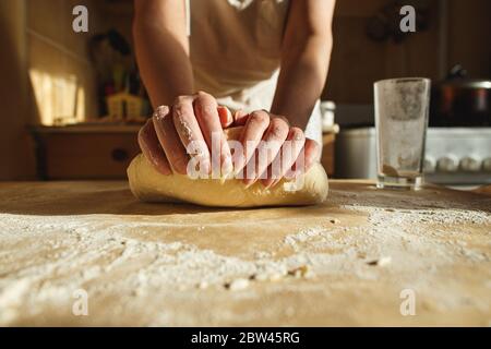 Die Hände der Frau kneten den Teig auf einem Tisch in warmem Sonnenlicht. Stockfoto