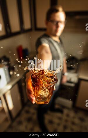 Ein Mann, der ein Glas Whiskey mit Spritzern in der Küche hält. Kreativer Halt. Stockfoto