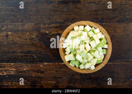 Zucchini in Würfel geschnitten in einem Holzteller auf einem braunen Holzhintergrund Stockfoto