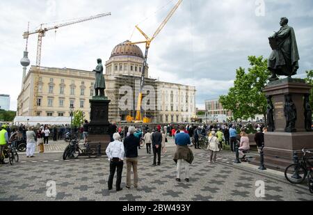 29. Mai 2020, Berlin: Zahlreiche Zuschauer beobachten beim Neubau des Berliner Schlosses, dem Humboldt Forum, wie die Kuppel mit dem Kreuz auf einem Sockel mit Engelsfiguren steht. Das ursprünglich ungeplante christliche Symbol auf dem Wiederaufbau des Palastes ist umstritten. Die erste Teileröffnung des Humboldt Forums, die für September geplant ist, wurde aus corona-Gründen verschoben. Das 644 Millionen Euro teure Gebäude soll jedoch noch in diesem Jahr eröffnet werden. Foto: Bernd von Jutrczenka/dpa Stockfoto