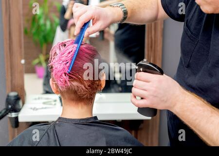 Rückansicht der Hände des Friseurs oder Friseurs, der Wasser auf das rosa Haar des Kunden im Friseursalon sprüht. Stockfoto