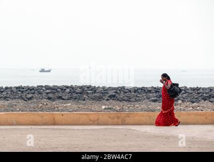 Somnath, Gujarat, Indien - Dezember 2018: Eine Inderin mit einem Sari geht alleine auf der Strandpromenade in der Stadt Somnath. Stockfoto