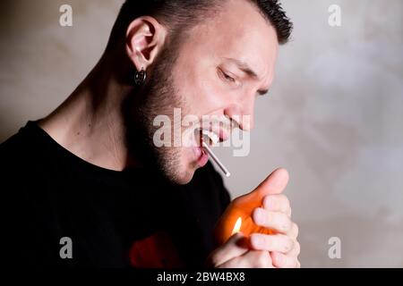 Ein Mann versucht scherzhaft, einen Stock mit lutschenden Süßigkeiten anzuzünden, die er in seinem Mund hält Stockfoto