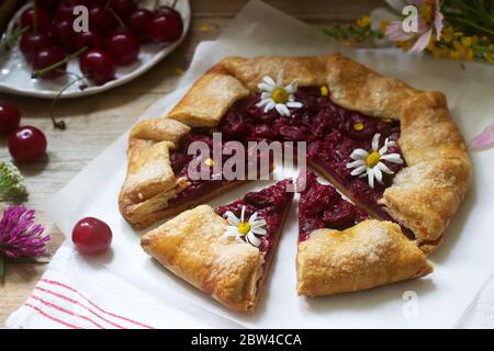 Süße Pie-Galette mit saftiger Beerenfüllung, Beeren und Wildblumen auf Holzhintergrund. Rustikaler Stil. Stockfoto
