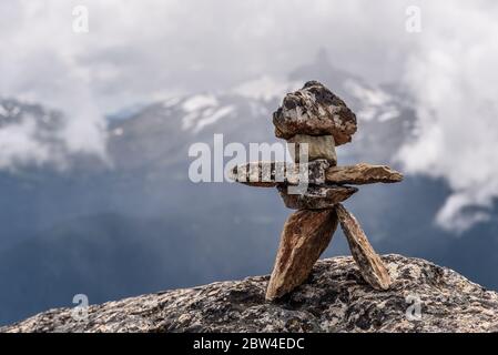 Eine Inukshuk Figur, steht auf der Spitze eines Berges, in Whistler, Kanada, mit Blick auf eine Berglandschaft. Stockfoto