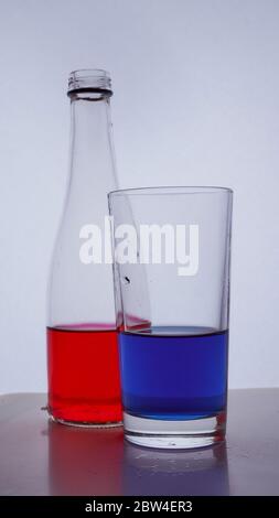 Flasche und Glas. In dem die roten und blauen Flüssigkeiten auf einen weißen Hintergrund gegossen werden Stockfoto