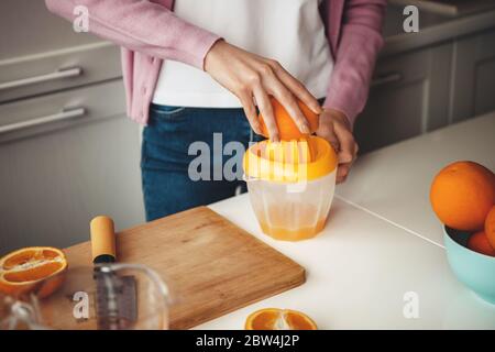 Nahaufnahme eines kaukasischen Dame, die mit einer Quetschpresse Saft aus Orange auf dem Tisch macht Stockfoto