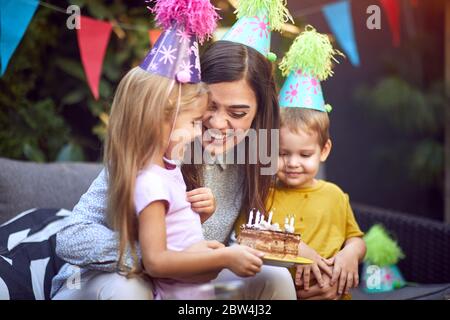 Lächelnde Mutter und ihr Junge und Mädchen Kind feiern Kinder Geburtstag Partei und Blasen Kerze c Stockfoto