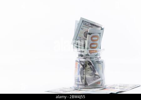 Glas voll und überfließend mit hundert Dollar Banknoten sitzen auf einem großen Haufen Geld. Weißer negativer Raum, Kopierbereich. Konzept spart Geld für Stockfoto