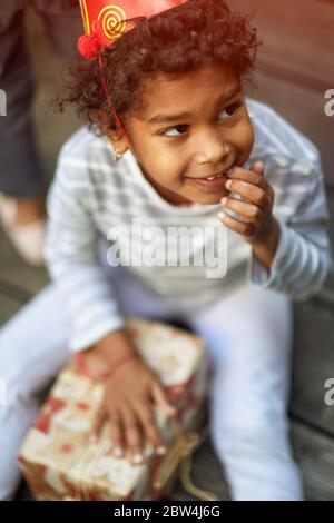 Kleine niedliche Afro-americangirl in Geburtstagsmütze hält Geburtstagsgeschenke. Stockfoto