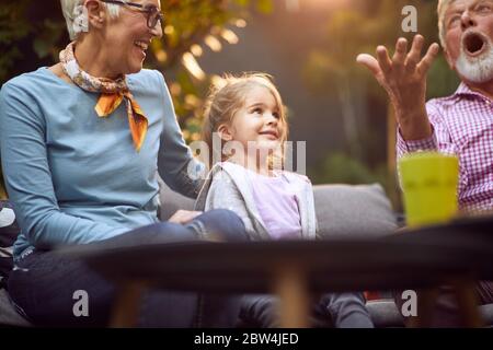 Großeltern spielen mit lächelnden Enkelin.Mädchen genießen mit ihren Großeltern draußen zu Hause. Stockfoto