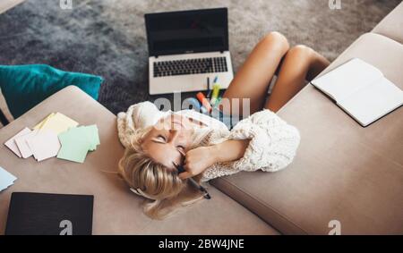 Müde kaukasische Dame mit blonden Haaren, die nach dem Online-Unterricht in der Nähe des Computers auf dem Boden ruht Stockfoto