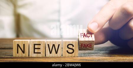 Ein Mann legt Holzblöcke mit den Worten News - Fakt oder Fake. Falsches / wahres Informationskonzept. Gelbe Drucktaste. Stockfoto