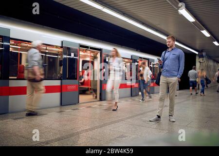 Junger entspannter Mann in einer U-Bahn schaut auf sein Handy, SMS, wartet. Stockfoto