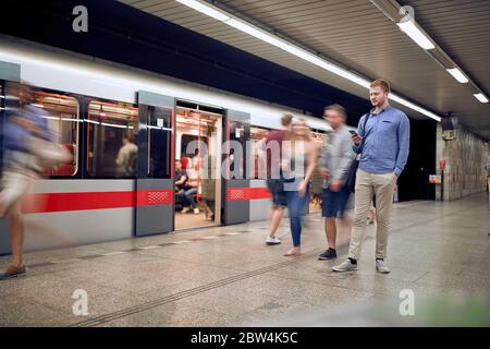 Junger entspannter Mann in einer U-Bahn, nicht in Eile, Blick auf sein Handy, SMS, Lesen, Senden, Nachricht, E-Mail. Urban Technology Konzept Stockfoto