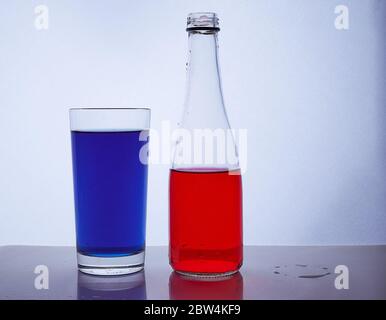 Flasche und Glas. In dem die roten und blauen Flüssigkeiten auf einen weißen Hintergrund gegossen werden Stockfoto