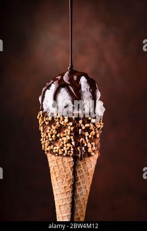 Eiscreme mit Tropfen geschmolzener dunkler Schokolade und gehackten Haselnüssen Stockfoto