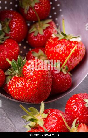 Im Vordergrund eine Gruppe von natürlichen, herzförmigen Erdbeeren in einem alten Sieb Stockfoto