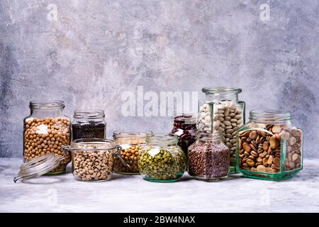 Große Auswahl an getrockneten Hülsenfrüchten in Gläsern. Graue Hintergrundstruktur Stockfoto