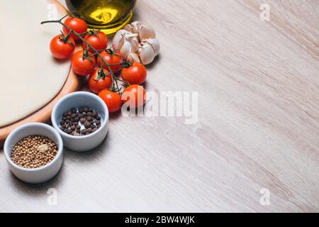 Teigbasis für die Pizza auf einem Holzbrett und Kirschtomaten, Olivenöl, Zwiebeln, Knoblauch. Stockfoto