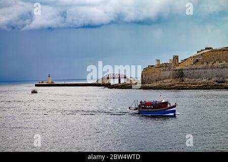 VALLETTA, MALTA - 2. OKTOBER 2019: An einem bewölkten Tag fährt ein Hafenschiff an der Brücke und am Leuchtturm vorbei. Stockfoto