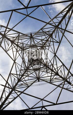 Stahlgitter Struktur eines Hochspannungsmast erzeugt ein geometrisches Muster gegen einen blauen Himmel mit Wolken. Stockfoto