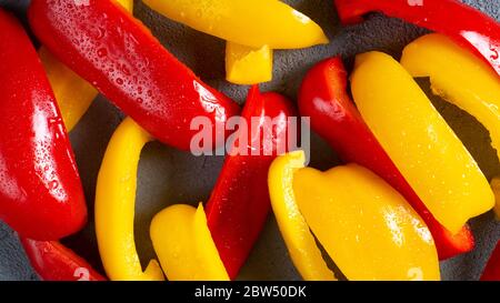 In Scheiben geschnittene Paprika für gesunde auf dunklem Hintergrund. Frisch gewaschene Scheiben Paprika. Rote und gelbe Paprika Stockfoto