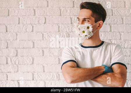Portrait des glücklichen männlichen Arzt im Sommer Schutzmaske halten die Arme gekreuzt und schauen Sie sich Kopierraum. Junger Mann trägt medizinische Gesichtsmaske mit Gänseblümchen Stockfoto