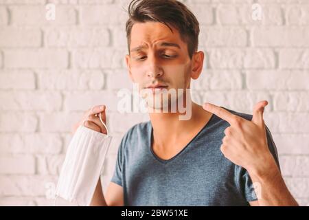 Porträt des jungen Hipster Mann mit roter Sonnenbrand Haut nach dem Tragen medizinischer Gesichtsmaske. Verwirrt Mann mit lustigen Sonne tan Linien auf Gesicht von schützenden fac Stockfoto