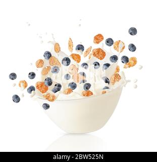 Getreide Cornflakes und Heidelbeeren fallen in Schüssel mit Milchspritzer. Gesundes Frühstück. Isoliert auf weiß Stockfoto