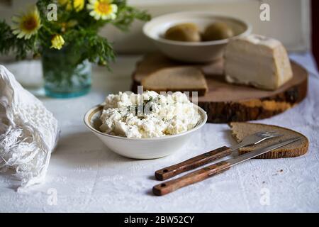 Frischer italienischer Ricotta mit Roggen selbstgebackenem Brot und Schmalz auf dem Tisch, rustikales Stillleben mit Frühlingsblumen Stockfoto