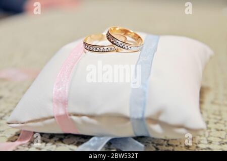 Gold und Silber Ring mit Relief unter einem weiteren kleineren Ring, die beiden Ringe auf einem schönen weißen Kissen mit blauen und rosa Details. Stockfoto