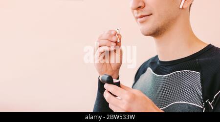 Nahaufnahme eines glücklichen Sportmanns, der Bluetooth-Kopfhörer ins Ohr legt und vor dem Hintergrund lächelt und mit Kopierfläche lachend ist. Junger Fitness-Mann Musik in w Stockfoto
