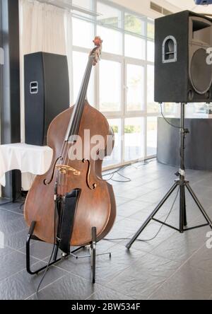 Alte hölzerne Kontrabass neben einem Lautsprecher in einem Innenraum ohne Menschen. Stockfoto