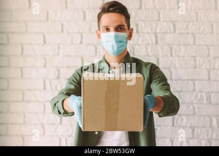 Happy Delivery Service Mitarbeiter in Schutzmaske, Gummihandschuhe geben Karton an den Kunden. Junge Hipster Mann Kurier in medizinischen Gesichtsmaske Auto Stockfoto