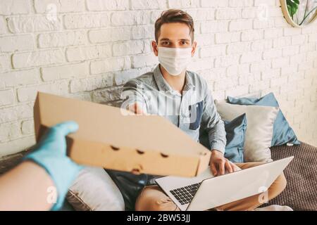 POV der Lieferservice Mitarbeiter in Schutzhandschuhe geben Karton Pizza Box an glückliche Kunden. Hipster Mann in medizinischen Gesichtsmaske erhalten italienische f Stockfoto