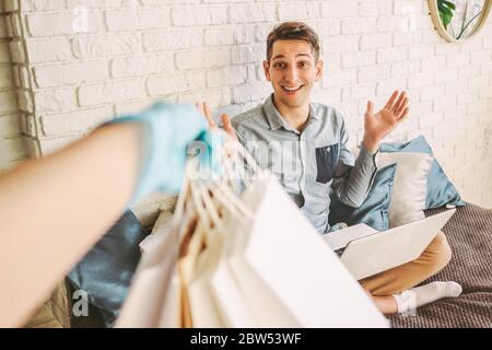 Glücklich Hipster Mann zu Hause arbeiten und Kauf Pakete aus dem Lebensmittelgeschäft zu erhalten. Lieferservice Kurier in Gummi Schutzhandschuhe geben Papier s Stockfoto