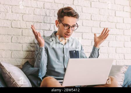 Junge erstaunt Geschäftsmann Blick in Laptop und aufgeregt fühlen, sitzen auf der Couch. Überraschte Hipster Mann in Brille Schock fühlen, während Computer verwenden. Mann, wow em Stockfoto