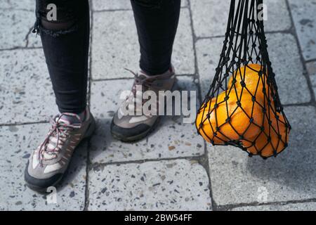 Junge Frau Füße und schwarzen Mesh-Tasche voller Orangen Früchte Stockfoto