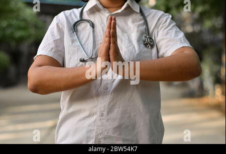 Porträt einer jungen medizinischen Facharbeiterin mit Stethoskop im Nacken, gekreuzte/gefaltete Hände in Namaste, um sich vor Corona Viru zu schützen Stockfoto