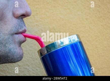 Nahaufnahme des Profils eines kaukasischen Mannes Nase und Mund, während er aus einem glänzend blauen Tasse durch ein rosa Stroh mit Kopie Raum schlürft Stockfoto