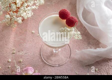 Ein Glas Ziegenkefir mit Himbeeren und Holunderblüten auf einem rosa Hintergrund Stockfoto